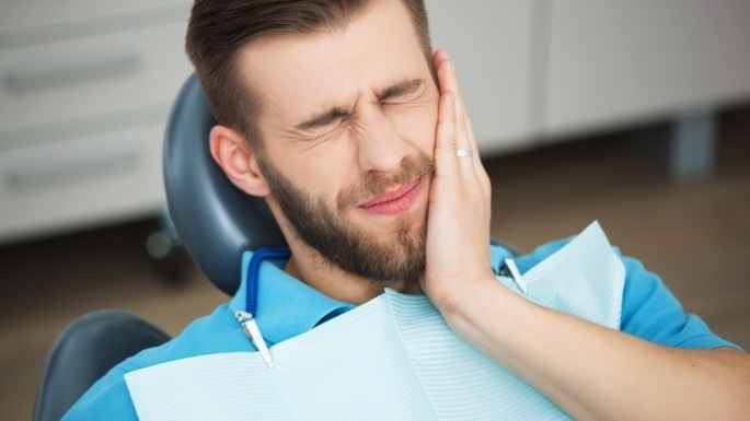 Man in dental chair holding his cheek in pain