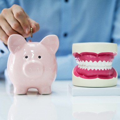A man putting a coin into a piggy bank next to a jaw mockup